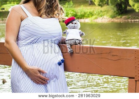 Pregnant Girl In Striped Dress With Toy For Her Infant. Hands And Belly Close Up