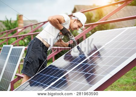 Back View Of Young Technician In Helmet Connecting Solar Photo Voltaic Panel To Metal Platform Using