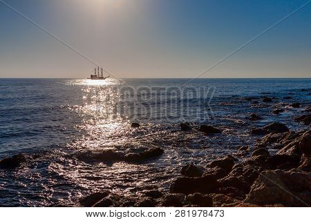Old Ship On The Horizon At Sea At Sunset. Stones In The Foreground