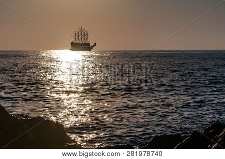 Old Ship On The Horizon At Sea At Gold Sunset. Stones In The Foreground