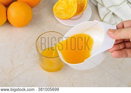Caucasian Woman Hands Pouring Freshly Squeezed Orange Juice From Manual Citrus Juicer Into A Glass O