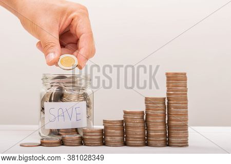 Hand Of Male Putting Coins In Jar With Money Stack Step Growing Growth Saving Money With Gray Backgr