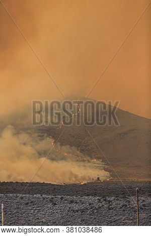 Orange Smoke From A Large Wildfire Over A Partially Burned Hill In The Desert