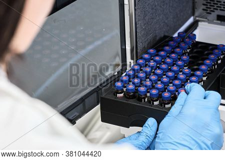 Scientist In A White Lab Coat Putting Vial With A Sample Into Autosampler Of Hplc System. High Perfo