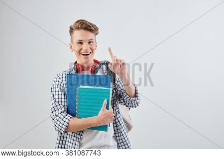 Studio Portrait Of Happy Excited Teenge Boy With Students Books In Hand Pointing Up In The Air And S