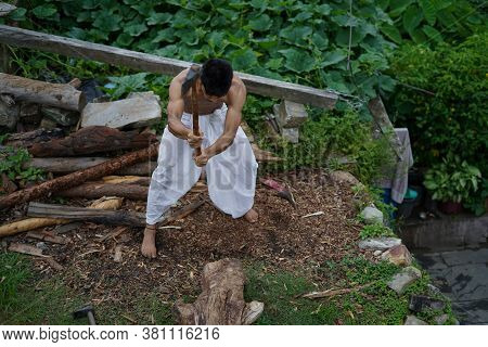 A Young Boy Wearing A White Dhoti Chopping Wood With An Axe.