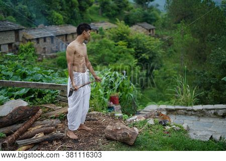 A Young Boy Wearing A White Dhoti Chopping Wood With An Axe.