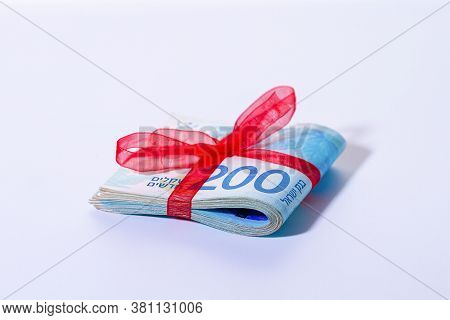 200 New Israeli Shekels Banknotes Are Folded In Half And Tied With A Red Ribbon On A Light Backgroun