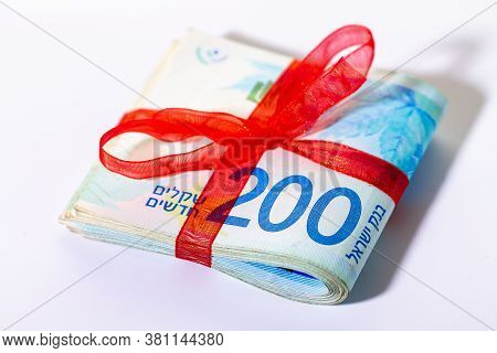200 New Israeli Shekels Banknotes Folded In Half And Tied With A Red Ribbon Close-up On A Light Back