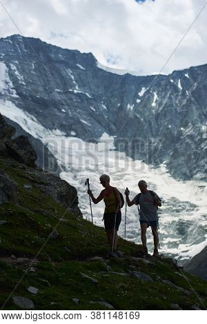 Zinal, Switzerland - July 19, 2019: Full Length Of Travelers With Trekking Sticks Walking Along Hill