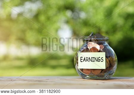 Earnings. Glass Jarglass Jar With Coins, On A Wooden Table, On A Natural Background. Investment And 