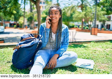 Young african american student woman smiling happy speaking on smartphone sitting on the grass at the university campus