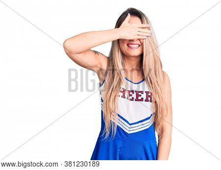 Young beautiful blonde woman wearing cheerleader uniform smiling and laughing with hand on face covering eyes for surprise. blind concept. 