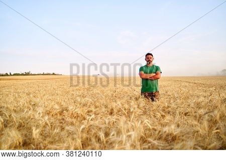 Happy Farmer Proudly Standing In Wheat Field With Arms Crossed On Chest. Agronomist Wearing Corporat