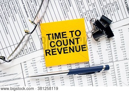 Text Time To Count Revenue On Financial Tables With Pen, Glasses And Paper Clips