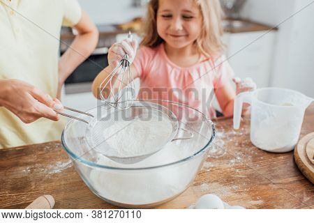 Cropped View Of Mother With Sieve And Daughter With Whisk Sieving Flour Into Glass Bowl, Selective F