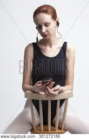 Ballet Concepts. Caucasian Female Ballet Dancer In Body Suit Sitting On Chair And Listening Music On