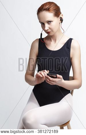 Portrait Of Female Ballet Dancer In Body Suit Sitting On Chair And Listening Music On Headphones. Ag
