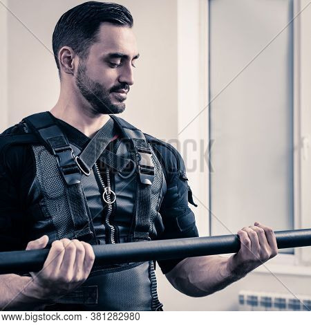 Portrait Of Young Sporty Man In Ems Suit Lifting Bar In Modern Gym