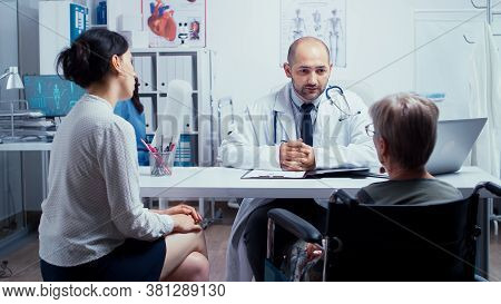Doctor Giving A Consultation For Elderly Disabled Woman With Her Daughter In Medical Office. Dsabled