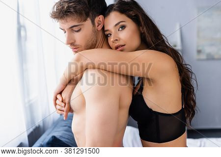 Sensual Woman In Bra Hugging Shirtless Boyfriend And Looking At Camera