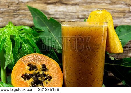 Papaya (carica Papaya) Juice Between Halved Fruits And Fresh Leaves