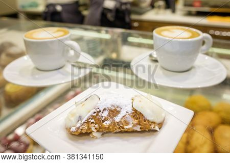 Two cups of cappuccino and fresh ricotta cannoli dessert close-up in coffee bar in Sicily, Italy. Cannoli is a traditional sicilian dessert