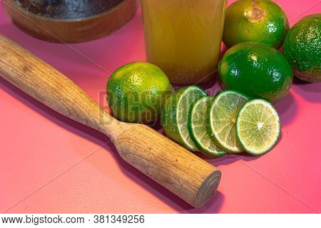 Lemon Juice And Lemonade (citrus Aurantifolia) Amid Wooden Pestle And Fresh Fruits On Pink Backgroun