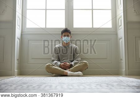 Young Asian Man In Quarantine Sitting On Floor Legs Crossed Looking At Camera