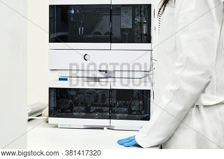 Scientist In Rubber Gloves And White Lab Coat Standing Near High Performance Liquid Chromatography H