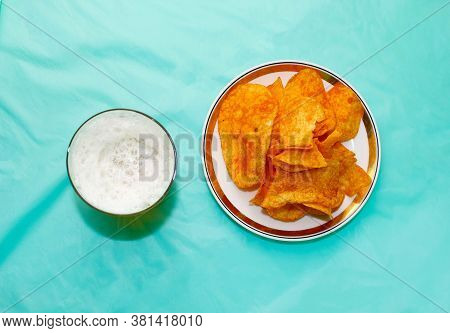 A Glass Of Beer And A Plate Of Chips On The Table With A Blue Background. The View From The Top.