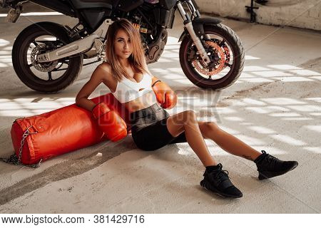 Pretty And Attractive Sportswoman Posing In A Light Studio Sitting On The Floor With A Large Orange 