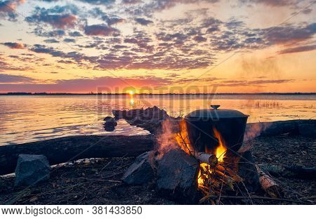 The Cauldron With Tea Is Boiled On The Fire. Weekend On The River. Dawn By The Water. Cooking Over A