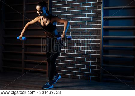 Full Lengh Image Of Athletic Young Woman Trains Her Shoulders Using Dumbbells In The Gym.