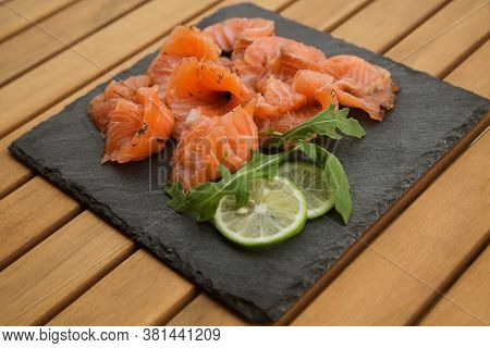 Slices Of Lightly Salted Salmon On A Black Plate Close Up On A Wooden Table.