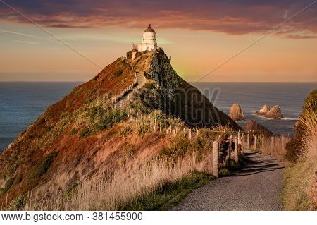 Vibrant Fire In The Sky And Cloudscape At Nugget Point Lighthouse At Dusk