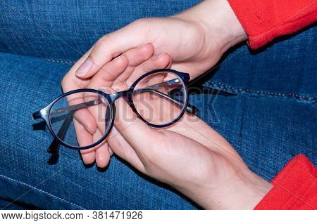 Close-up Of Human Hands Holding Blue Rimmed Glasses On Their Knees. Eyes Rest From Glasses. Glasses 