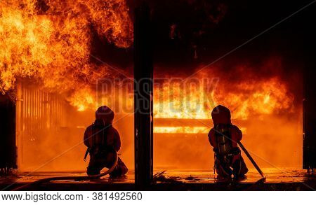 Firefighters using water fog fire extinguisher to fighting with the fire flame in large building. Firefighter and industrial safety disaster and public service concept.