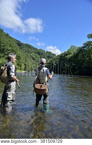 A father and his son fly fishing in summer on a beautiful trout river with clear water