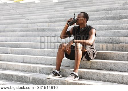 Thursty Black Male Athlete Drinking Water, Resting On Urban Stairs After Training Outdoors, Copy Spa