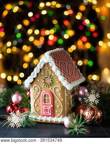 Gingerbread House With Pine Branches, Chrismtas Decorations And Chrismtas Lights In Background, Sele