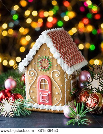 Gingerbread House With Pine Branches, Chrismtas Decorations And Chrismtas Lights In Background, Sele