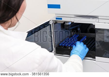 Scientist In A White Lab Coat Putting Vial With A Sample Into Autosampler Of Hplc System. High Perfo