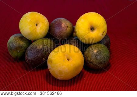 Pasiflora Fruits And Large Yellow Plums On Red Cloth Napkin Background, Closeup , Selective Focus