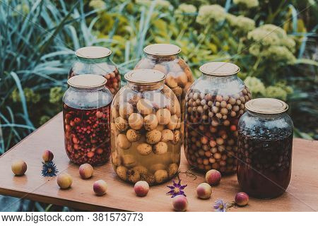 Jars With Kompot On Table. Sealed Glass Jars With Kompot Placed On Table Near Flowers And Fruits On 