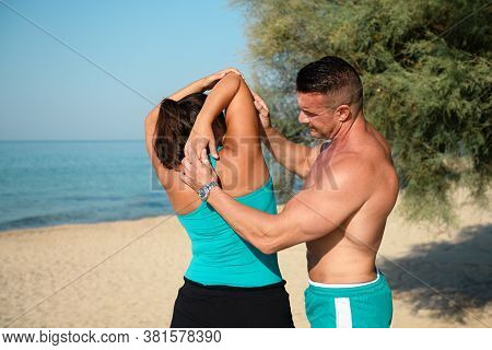 Trainer Helping A Fit Young Womann To Do Stretch Her Arms On The Beach After Workout. Yoga Closer To