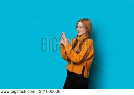 Ginger Caucasian Woman With Freckles Wearing Eyeglasses Is Chatting On Phone And Smile On A Blue Wal