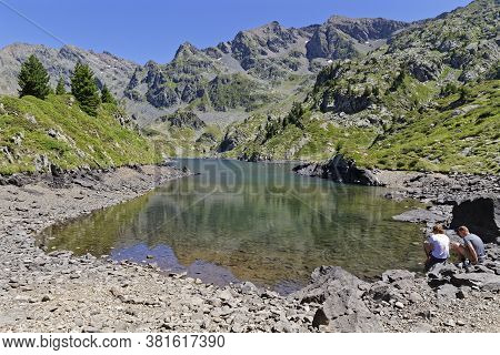 La Pra, France, August 6, 2020 : A Young Couple Of Hikers Rest For A While On The Shoreline Of A Bea