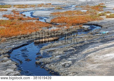 Spilled Streams Of Liquid Crude Oil Flow Down Drainage Ditch Into Public Body Of Water. Environmenta