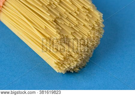 Raw Spaghetti Bunch On Blue Background With Copy Space.
